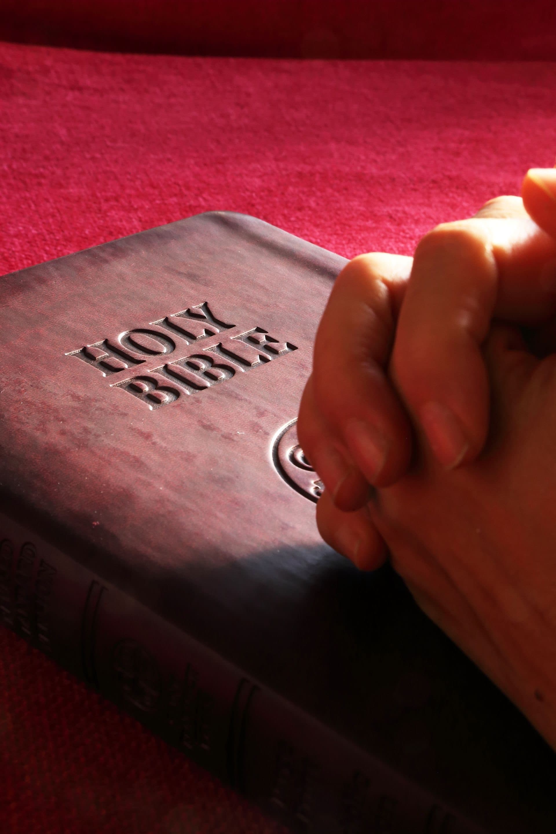 Hands folded in prayer resting on a Bible